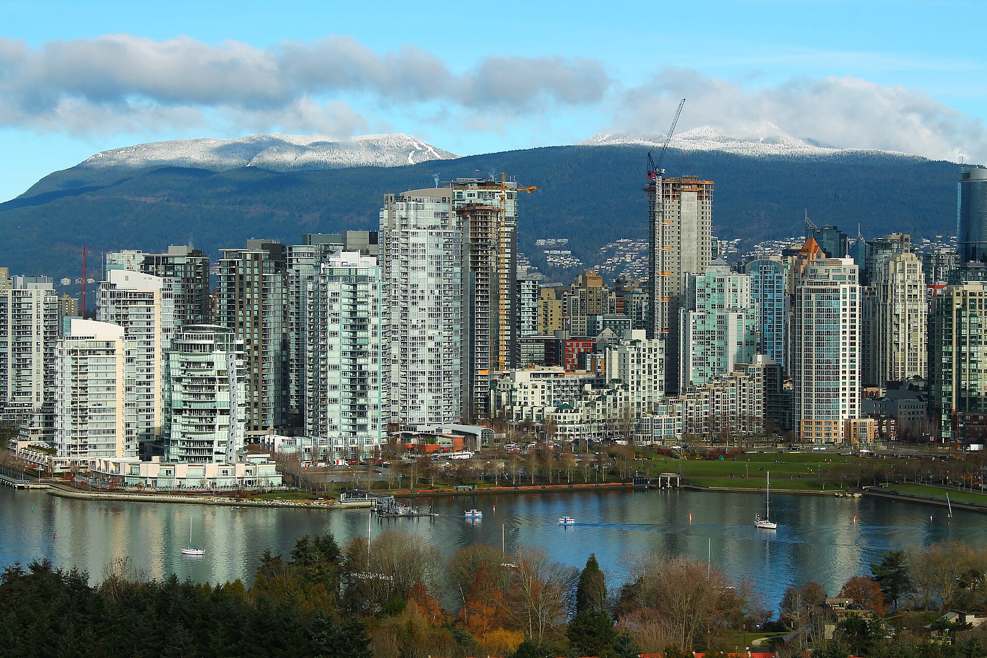 High-rise condominium towers along False Creek in Yaletown, Vancouver, with mountains behind.